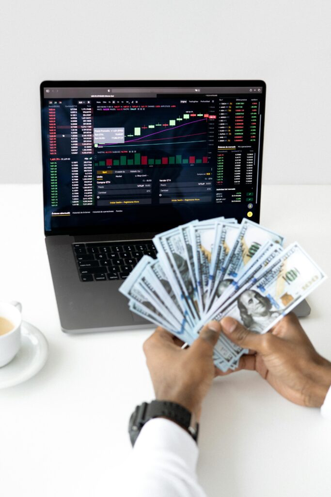 Hands holding cash in front of a laptop displaying stock market data, symbolizing financial growth and investment.